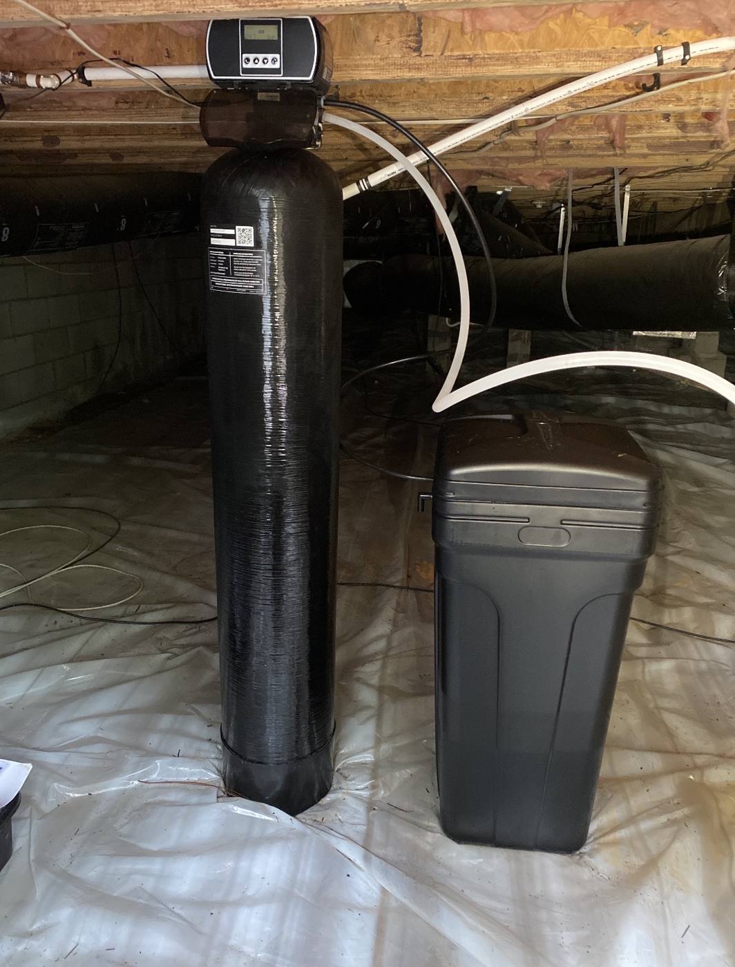 Iron filter and water softener system with brine tank installed in a Moore County crawlspace by On Point Plumbing